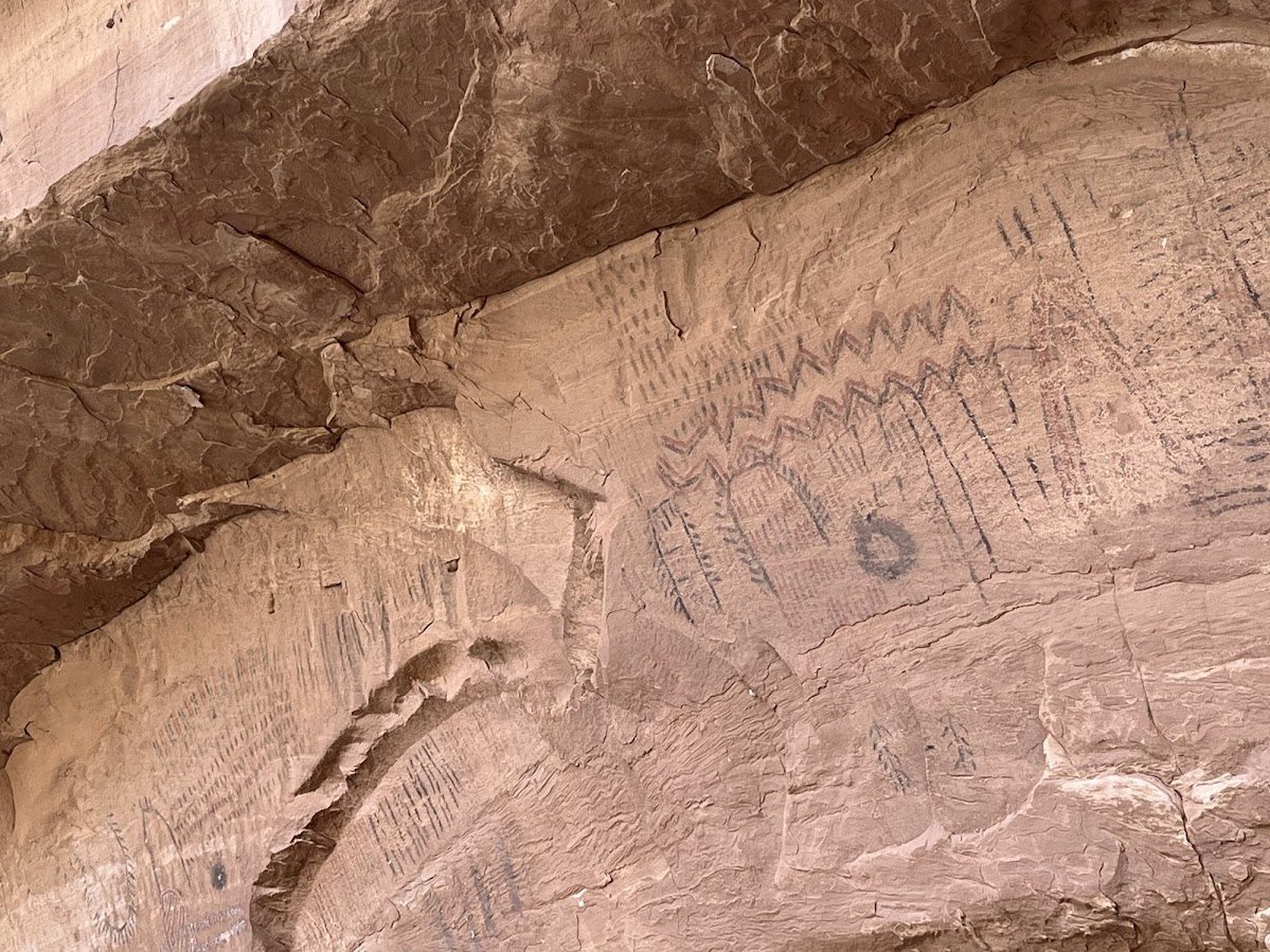 Faded linear and zigzag rock art on a sandstone wall.