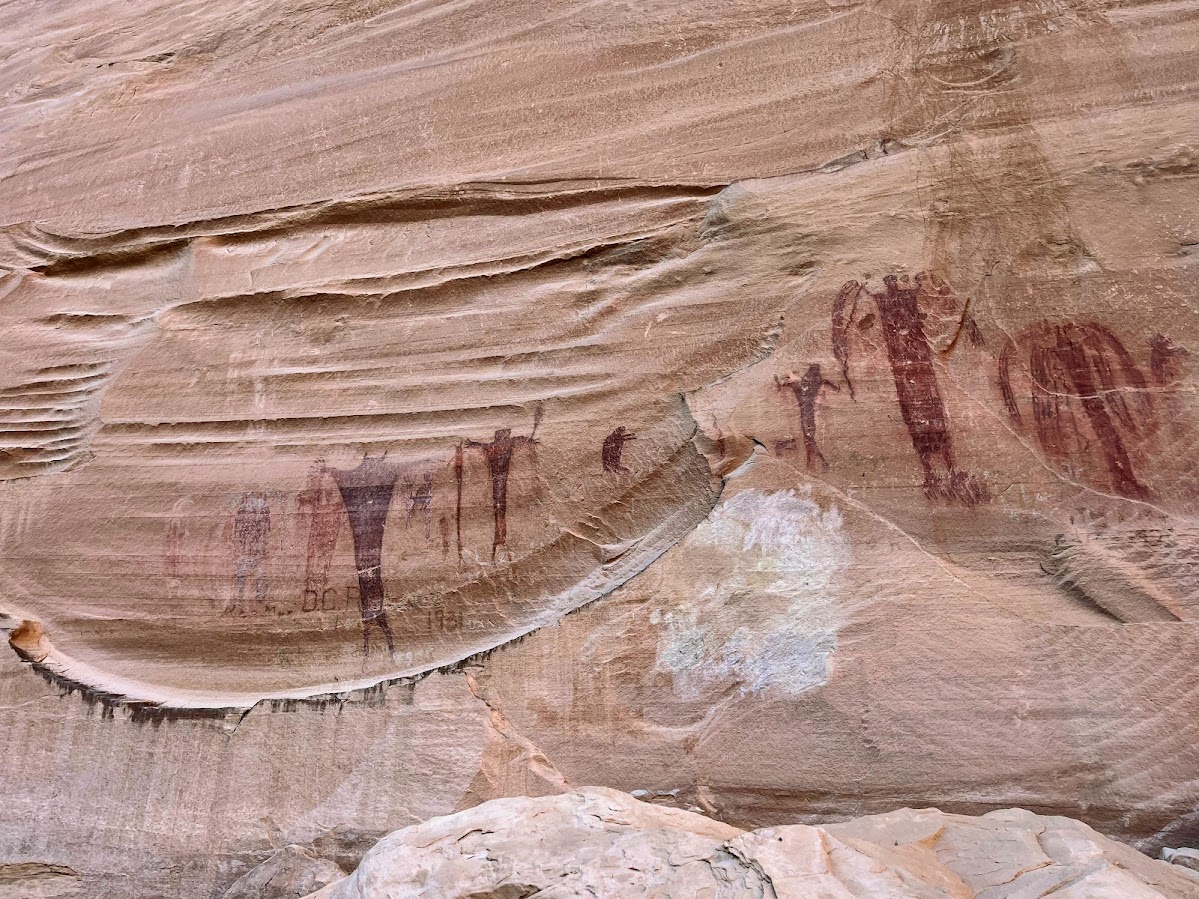 Row of faded pictograph figures on swirled sandstone.